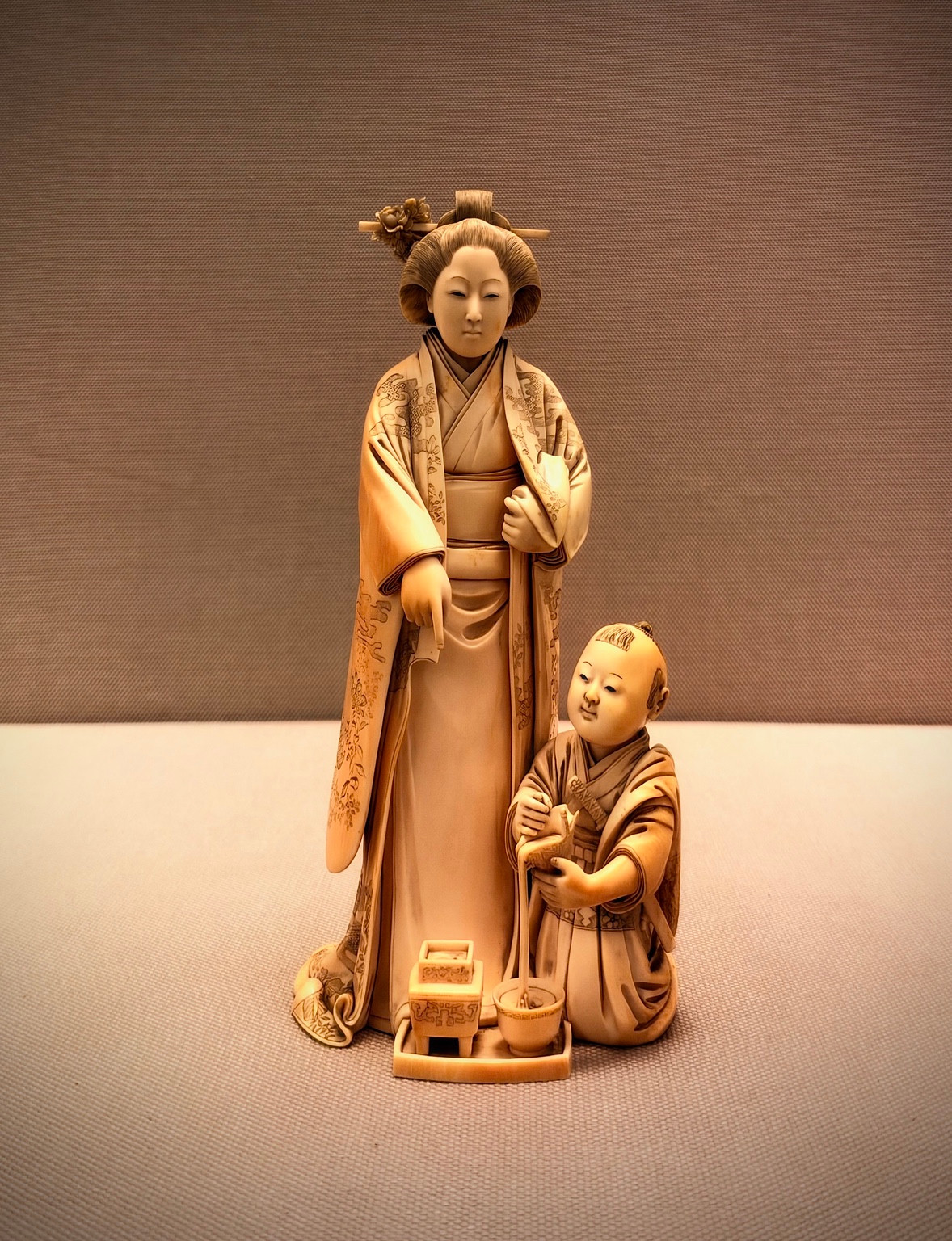 A detailed pale figurine of a woman and child in patterned robes, displayed against a plain background.