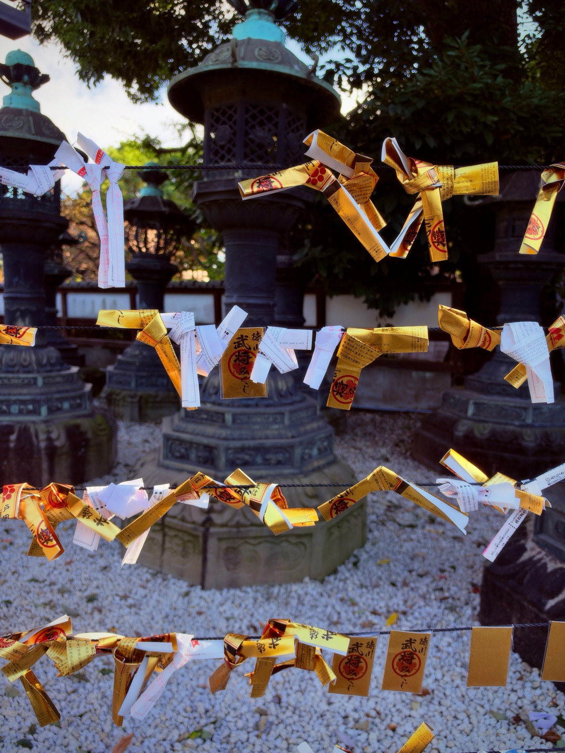 Gold and white paper slips tied to horizontal cords in front of large metal lanterns.