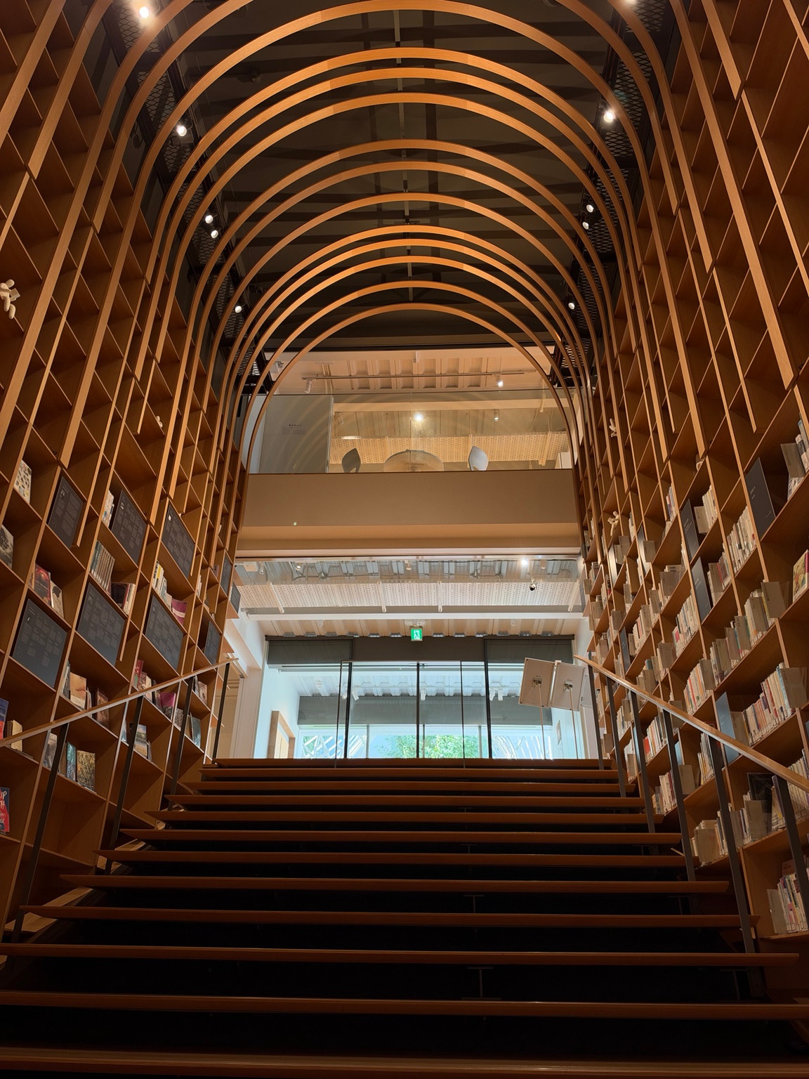 Looking up the book-lined stairs beneath curved timber ribs inside the Murakami Library.