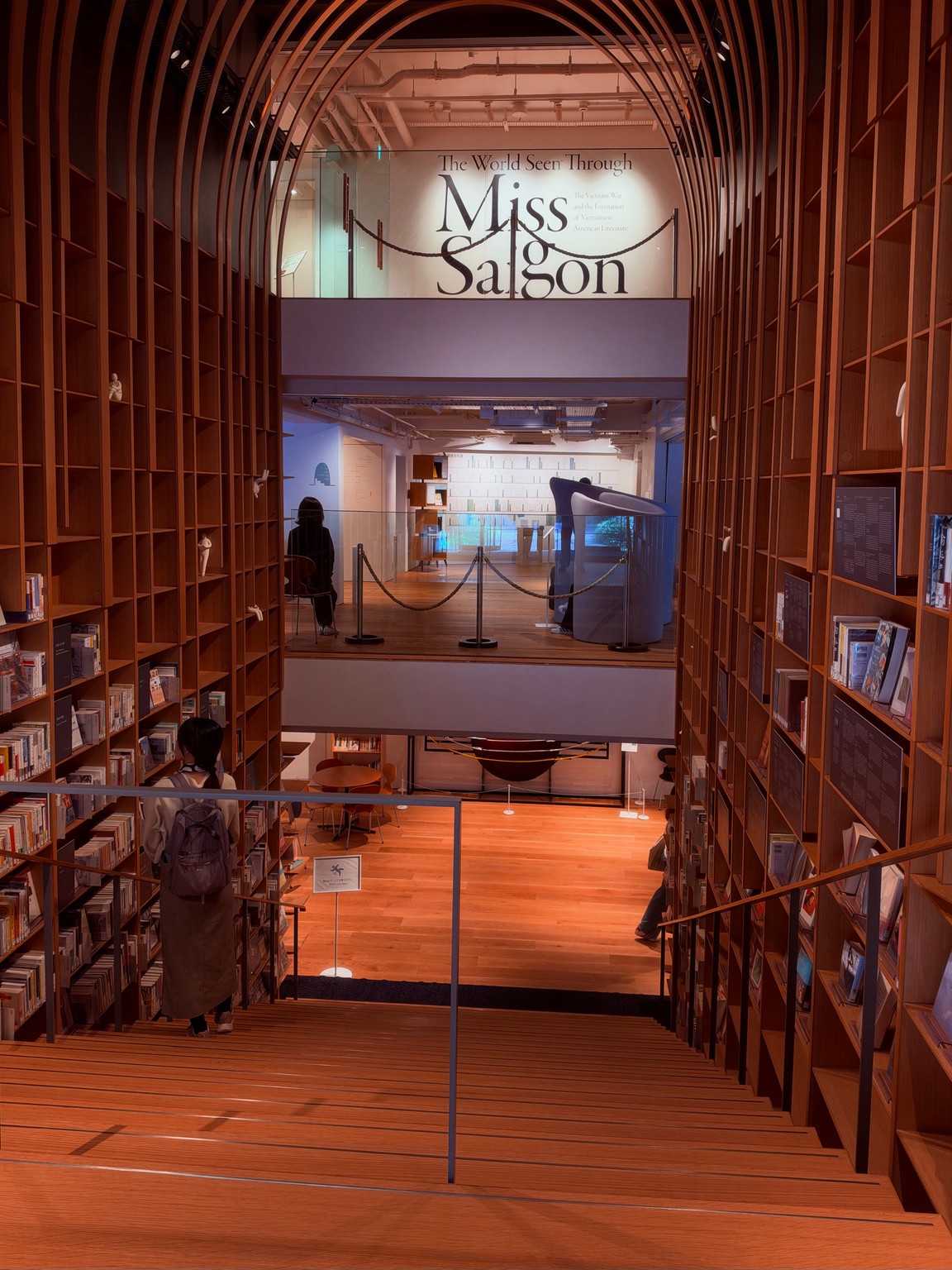 Looking down a wooden staircase lined with bookshelves and arching timber ribs inside the Murakami Library.
