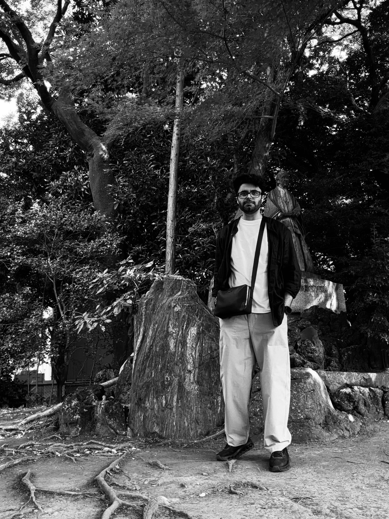 Black-and-white portrait of Bharat standing among trees and rocks, with a statue behind him.