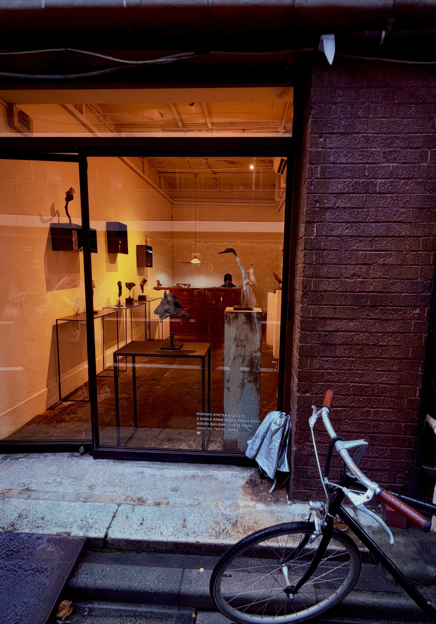 Warmly lit Morioka Shoten storefront with a bicycle against the dark brick façade.